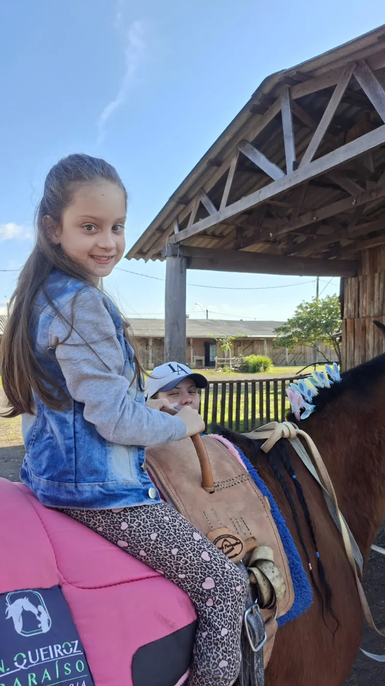 Menina sorrindo montada em cavalo com sela rosa