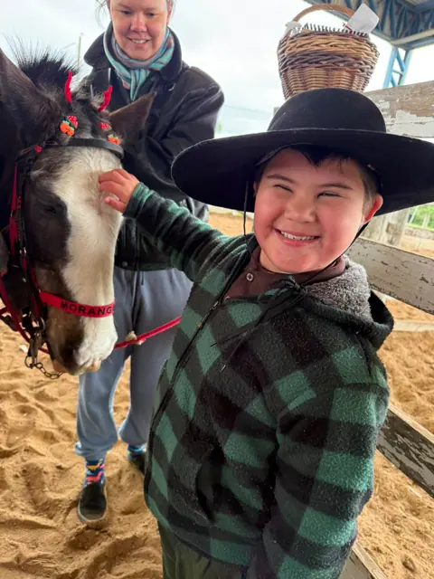Menino de chapéu sorrindo ao acariciar o cavalo