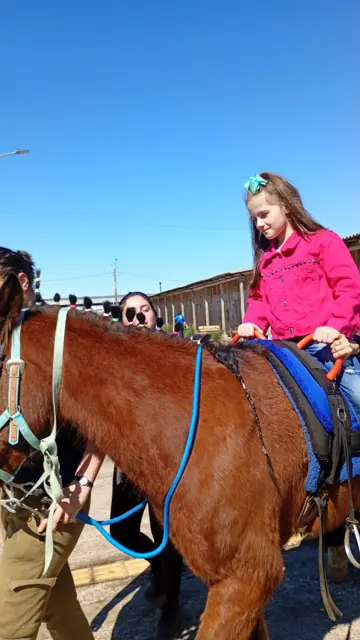 Menina de jaqueta rosa sorrindo a cavalo