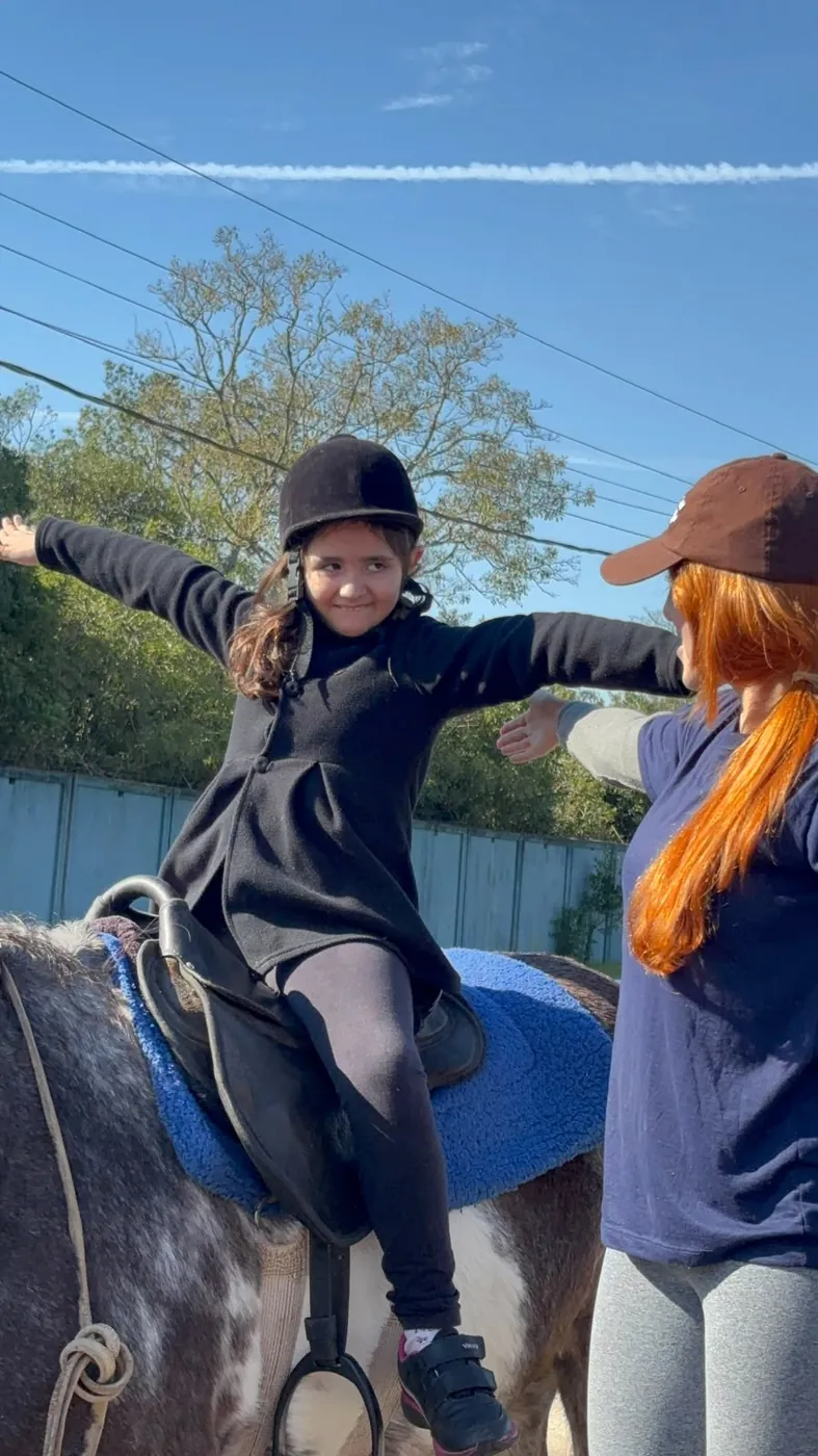 Menina de capacete montada a cavalo, de braços abertos, equilibrando-se