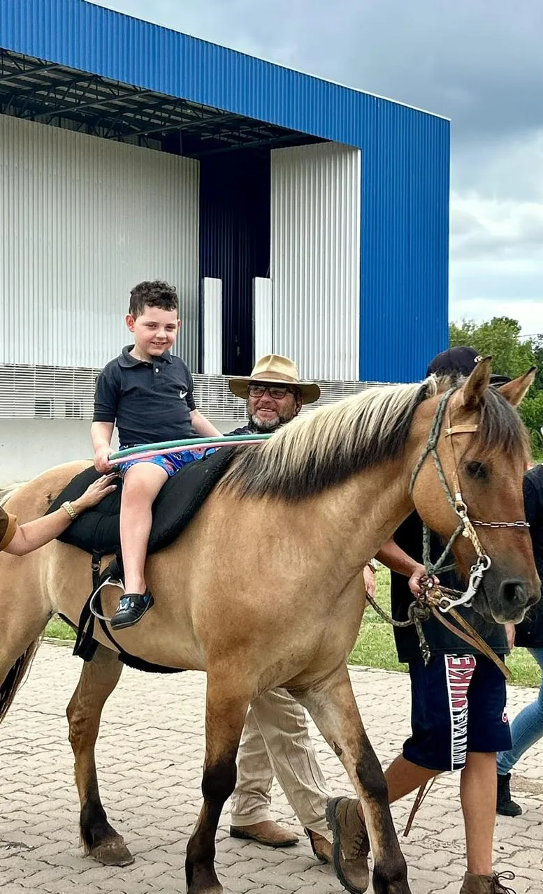 Menino sorrindo, montado em cavalo, acompanhado por profissionais da equipe