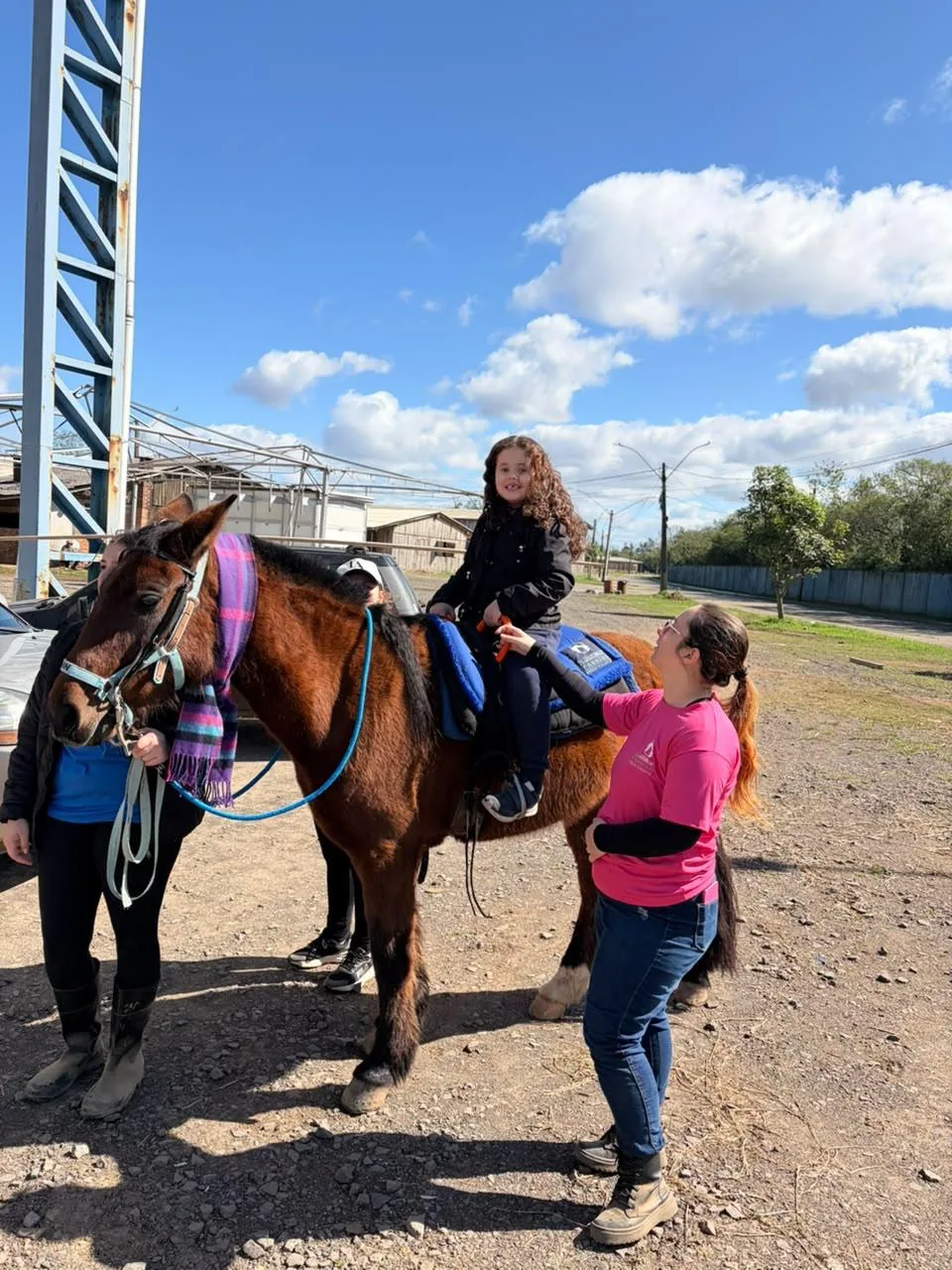 Menina montada em cavalo, com a equipe ao redor ajudando e acompanhando